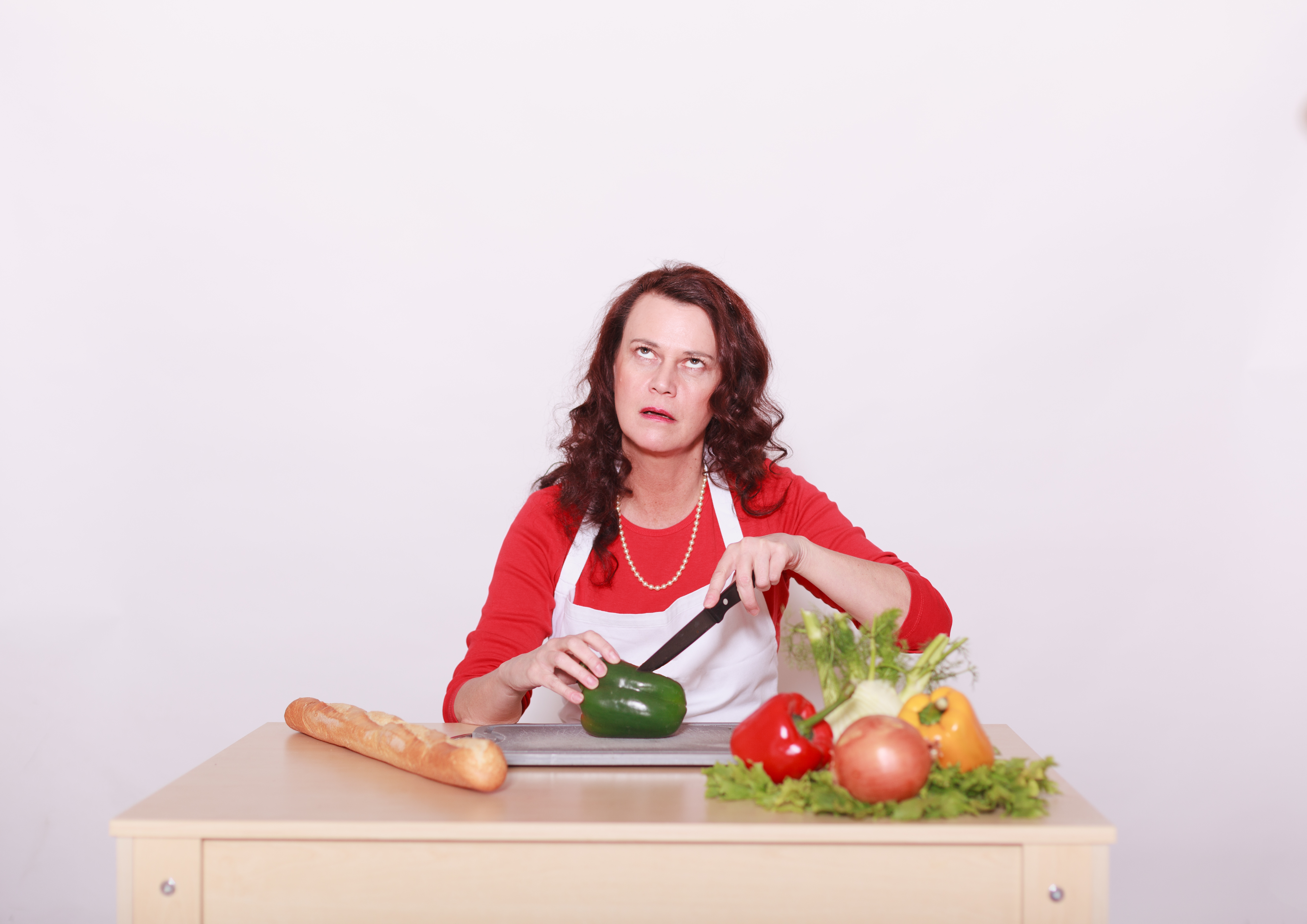 Kvinne med misfornøyd uttrykk i ansiktet som skjærer opp grønnsaker 