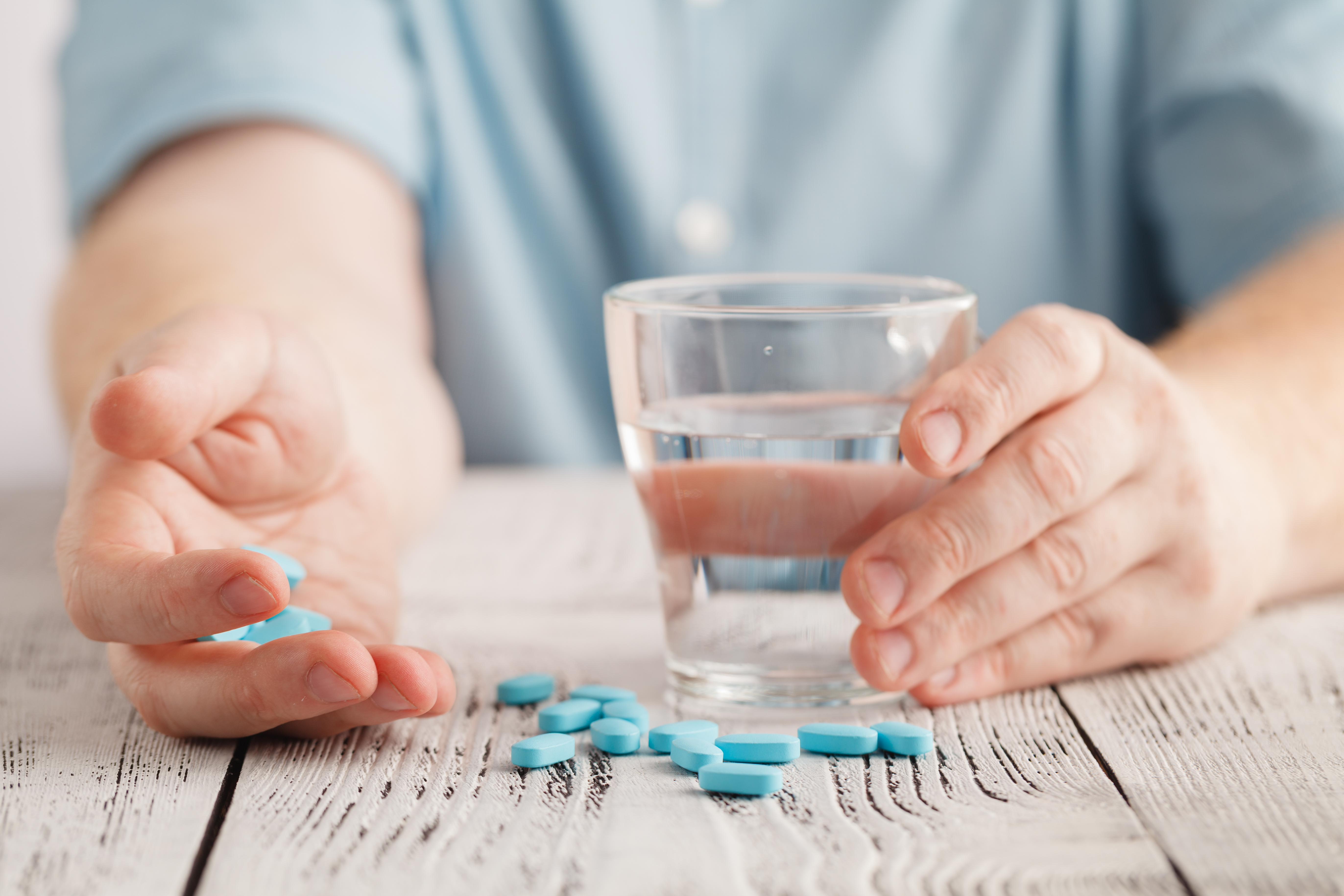 Illustrasjonsfoto av piller på bord, hånd som holder piller, og i andre hånd et vannglass.