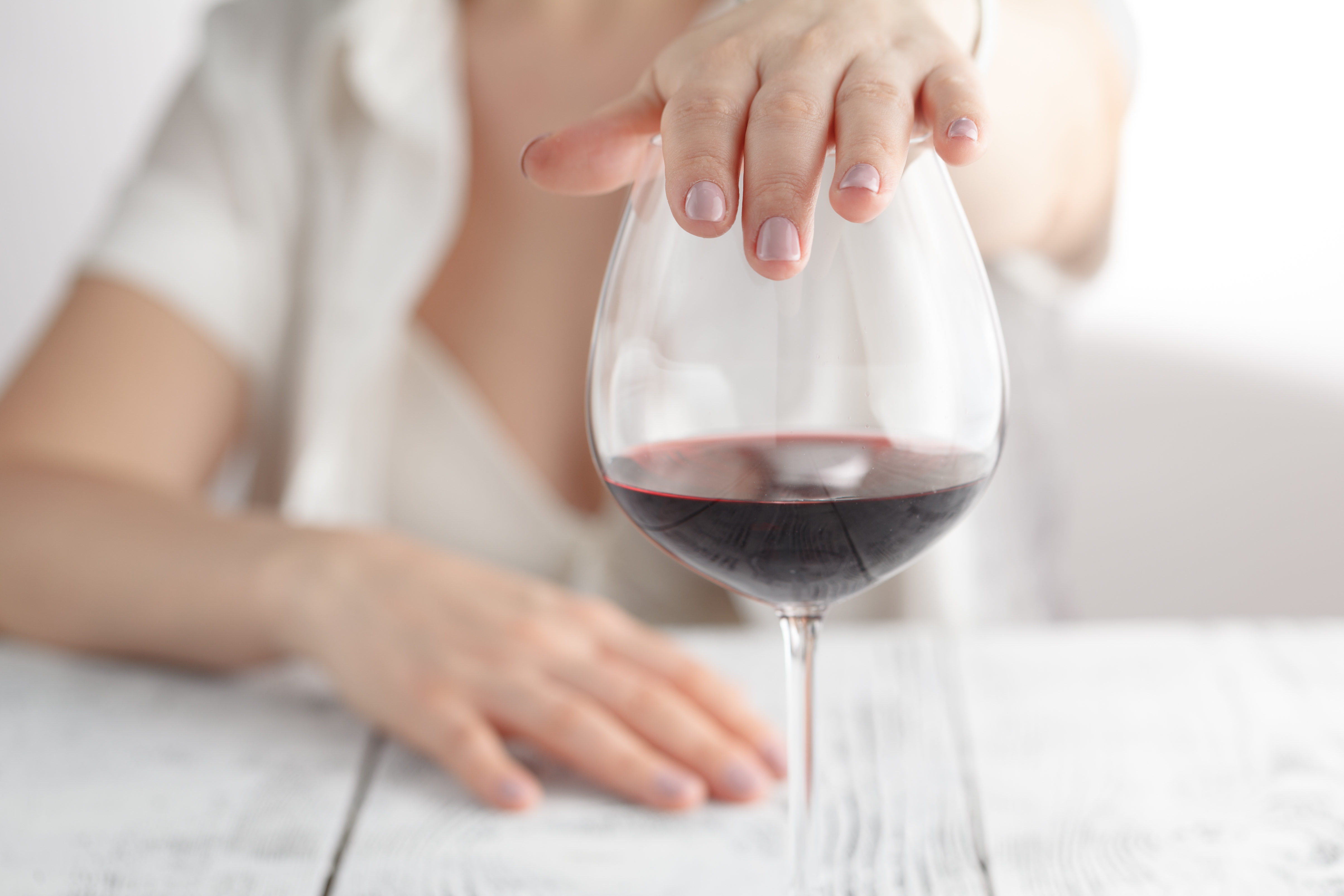 Kvinne som holder hånden over et glass rødvin