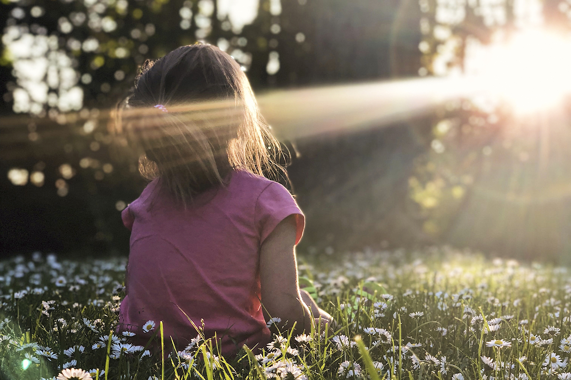 Illustrasjonsbilde av liten jente som sitter i gresset og ser mot solen