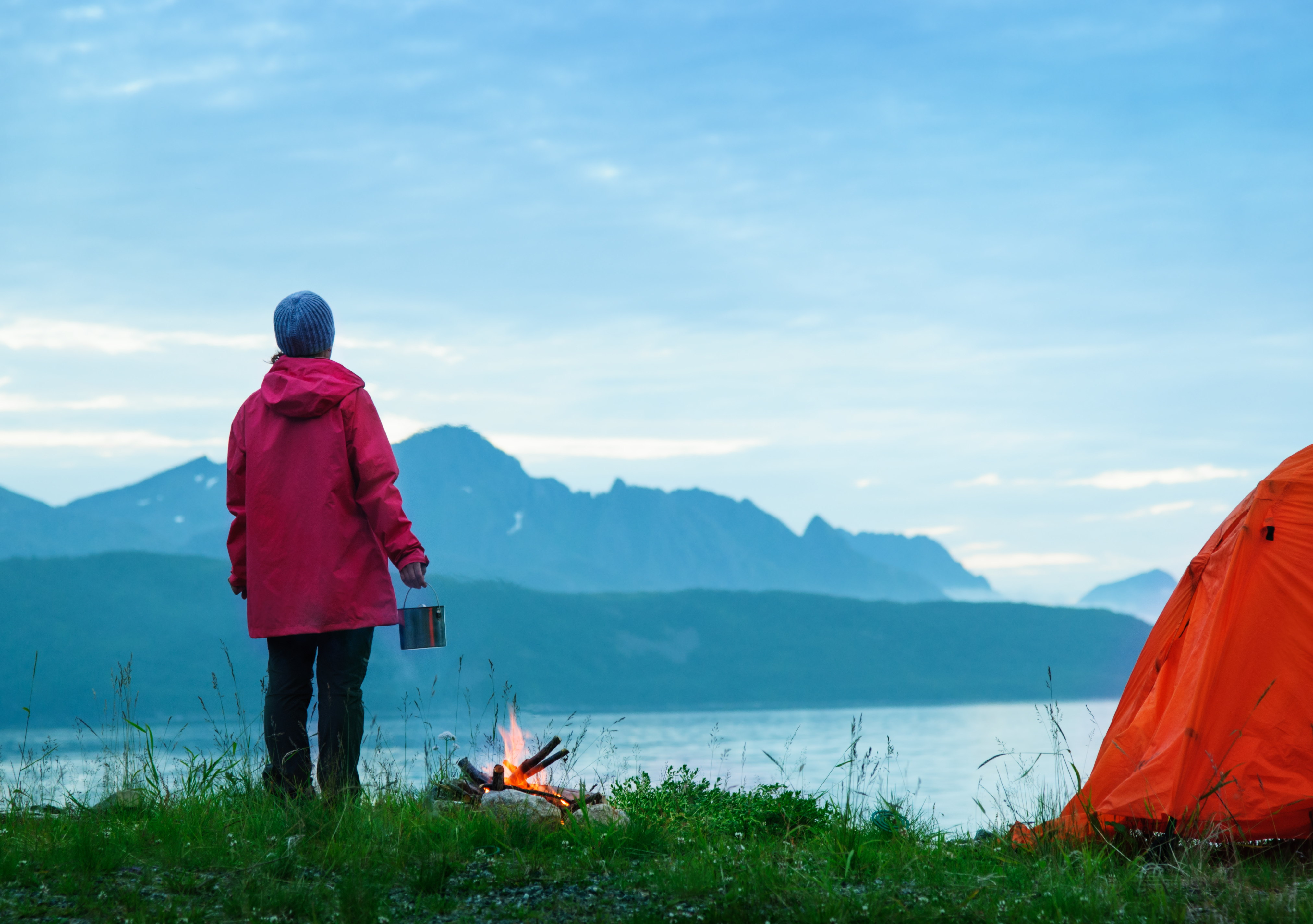 Kvinne på telttur ser ut over fjord og fjell. 