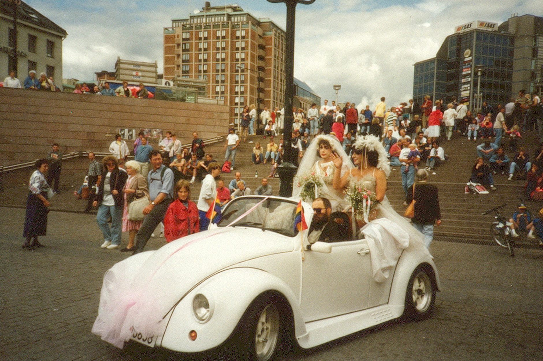 bilde av to personer i brudekjole sammen i åpen bil. 