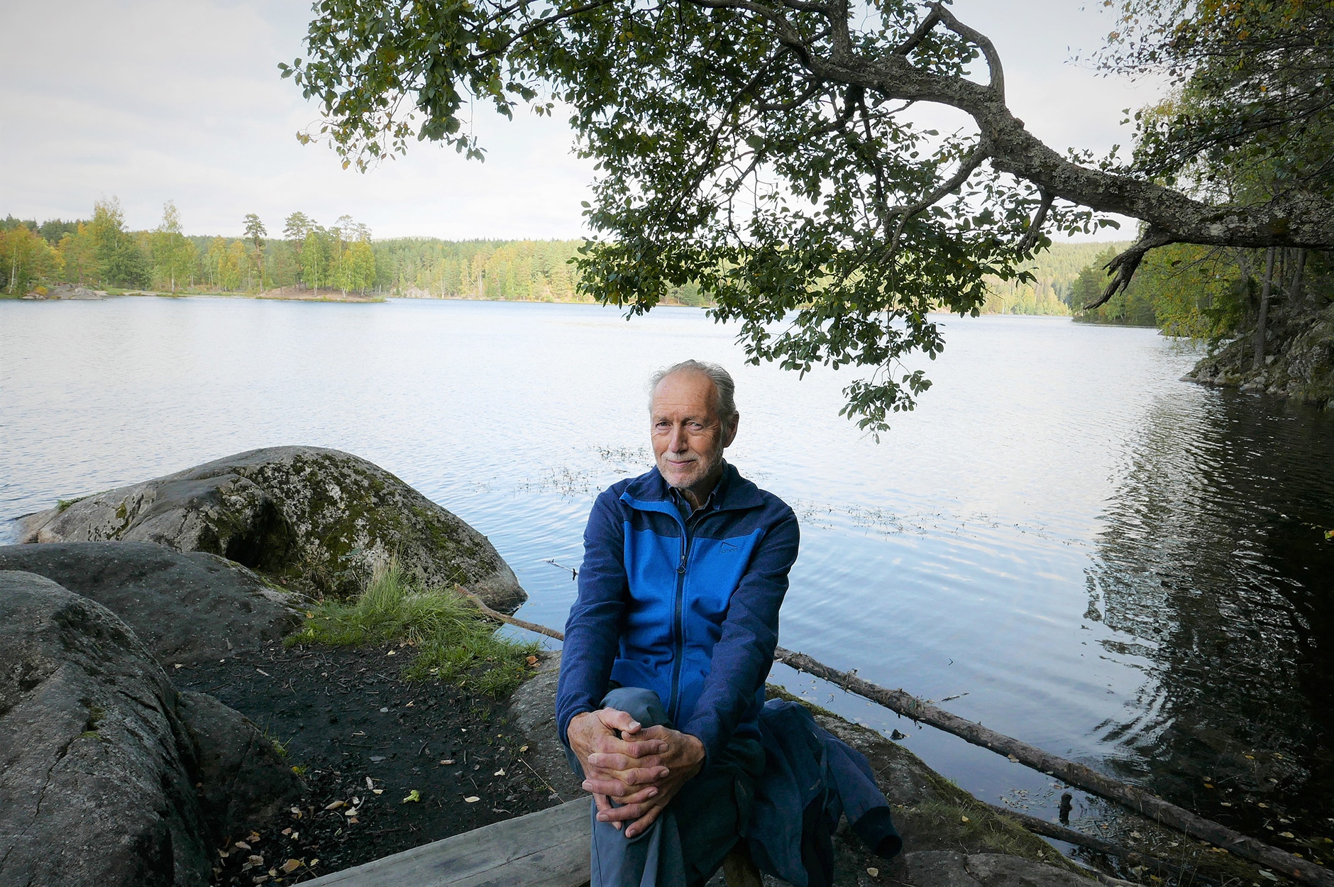 Portrett av Sigmund Hågvar som sitter på en stein i skogen