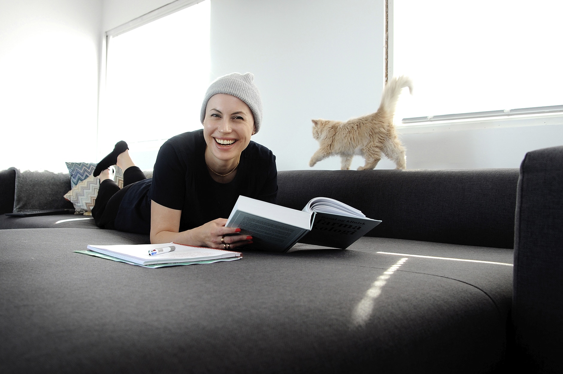Bilde av Julia Viita som ligger og leser på sofaen med en katt i bakgrunnen